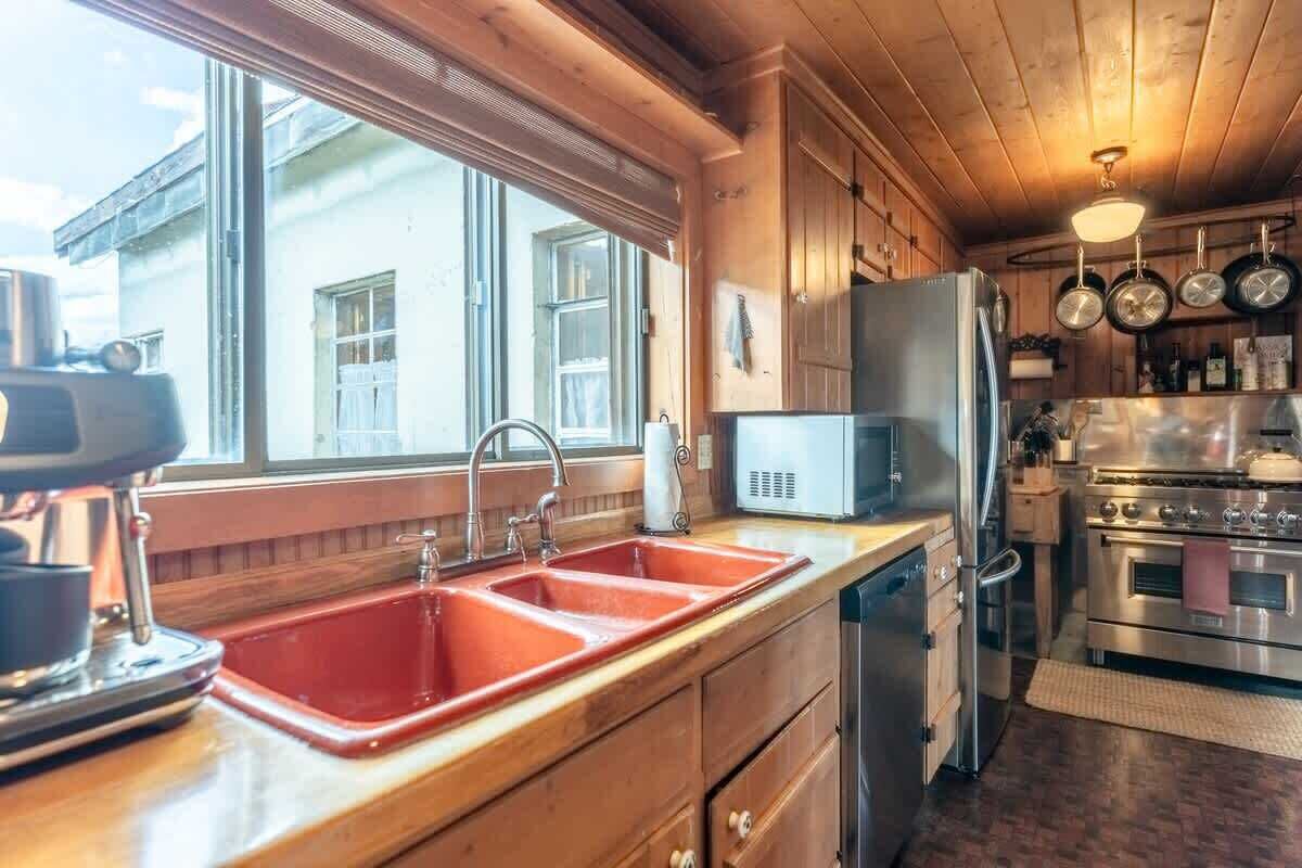 A kitchen with wooden cabinets, a red sink, a microwave, and a stove.