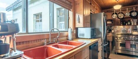 A kitchen with wooden cabinets, a red sink, a microwave, and a stove.