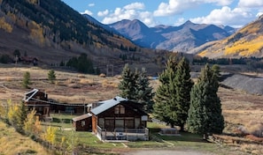 A cabin with a porch, surrounded by mountains and trees.