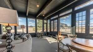 A room with a sofa, a table, and chairs, large windows with a view of the mountains. - The Steakhouse (Crested Butte)