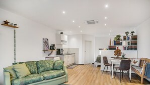 A modern living room with a sofa, a dining area with chairs, a kitchen with cabinets, and a bookshelf. - Studio Apartment 'Eifelzauber' with Shared Terrace, Wi-Fi and Air Conditioning (Greimerath)