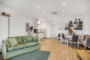 Una sala de estar moderna con un sofá, un comedor con sillas, una cocina con armarios y una estantería.
