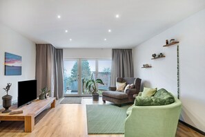 A modern living room with a flat-screen TV, a sofa, a chair, a coffee table, and a potted plant. - Studio Apartment 'Eifelzauber' with Shared Terrace, Wi-Fi and Air Conditioning (Greimerath)