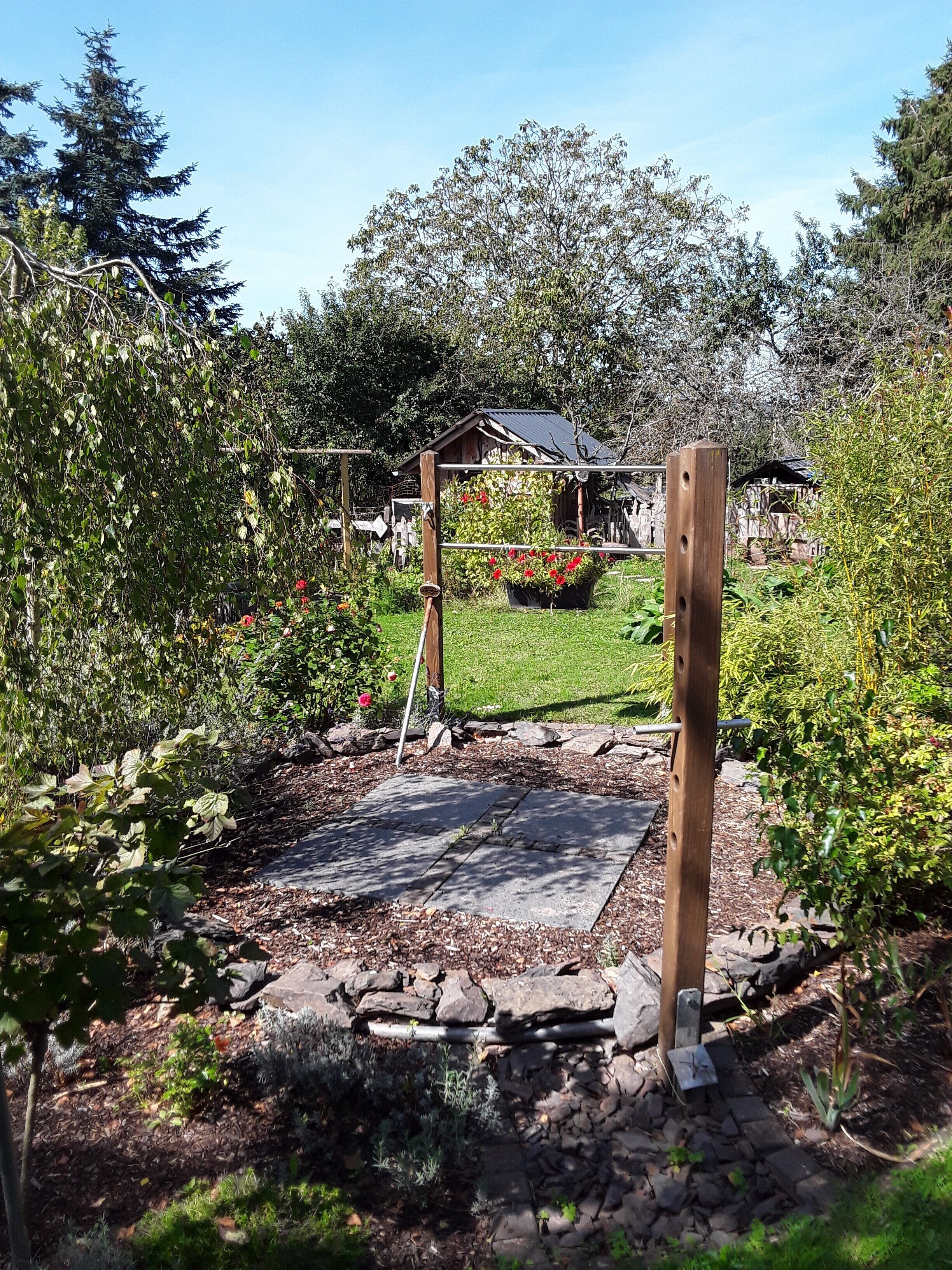 Un giardino con una pergola in legno, un vialetto in pietra e diverse piante.