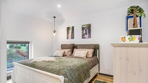 A bedroom with a bed, a window, a wall-mounted shelf with books and a plant, and a painting. - Studio Apartment 'Eifelzauber' with Shared Terrace, Wi-Fi and Air Conditioning (Greimerath)