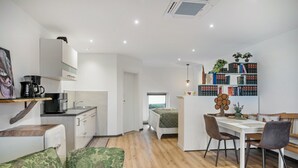 A modern kitchen with a coffee maker, a dining area with a table and chairs, and a bookshelf with books and plants. - Studio Apartment 'Eifelzauber' with Shared Terrace, Wi-Fi and Air Conditioning (Greimerath)