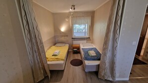 Une petite chambre, de taille modeste, comprenant deux lits simples, une petite table et une fenêtre donnant sur un paysage verdoyant.