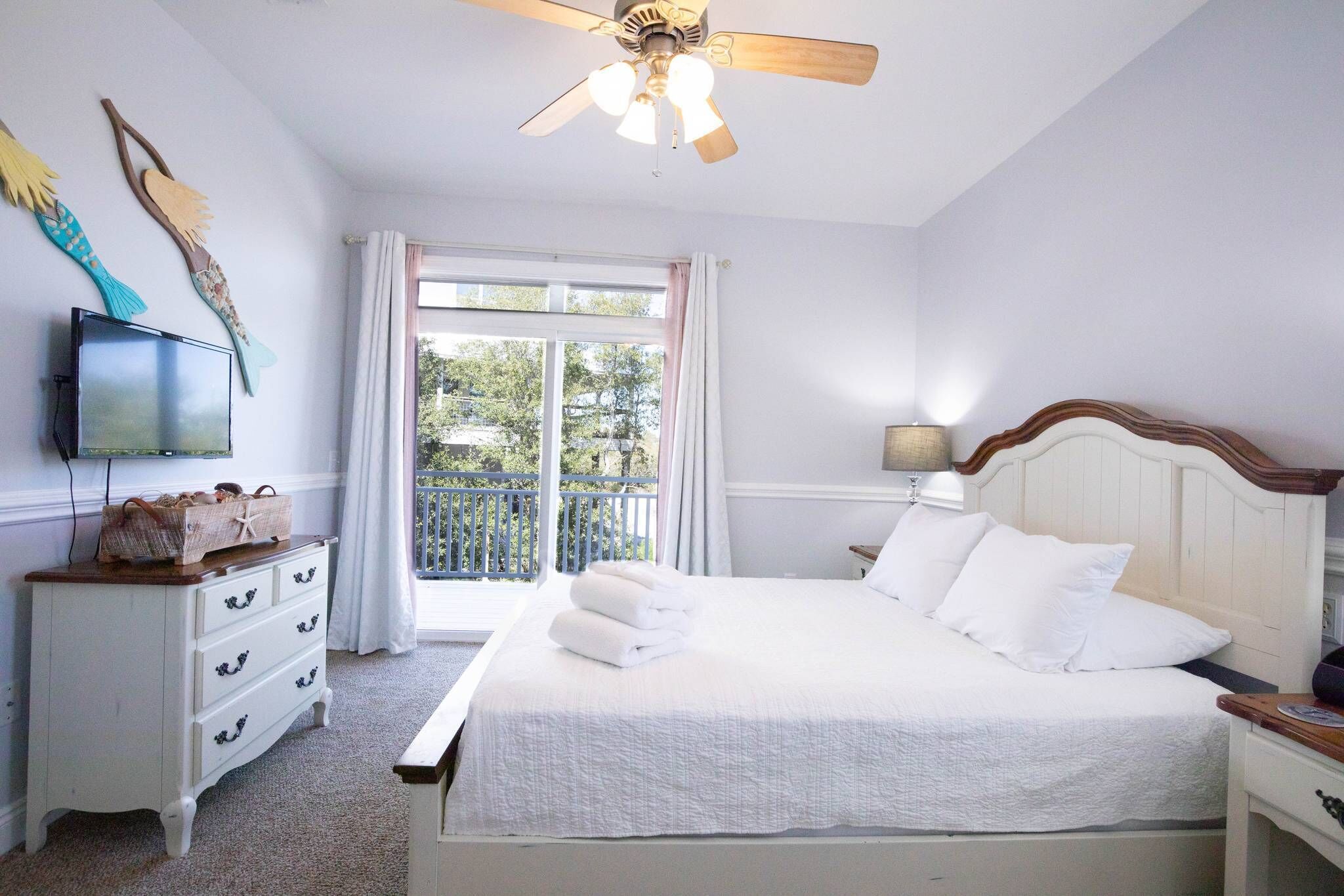 Une chambre à coucher comprenant un lit, une commode, un téléviseur et un balcon avec des rideaux.