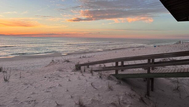 Ein Strand mit einer Holzstege, der zum Ufer führt, mit Blick auf den Ozean bei Sonnenuntergang.