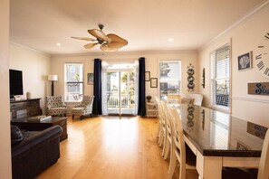 A spacious living room with a ceiling fan, a dining area with a glass table, and a view through a glass door to the outside. - Welcome to Sea Shed – Private Pool, Fire Pit, Pet Friendly (Cape San Blas)