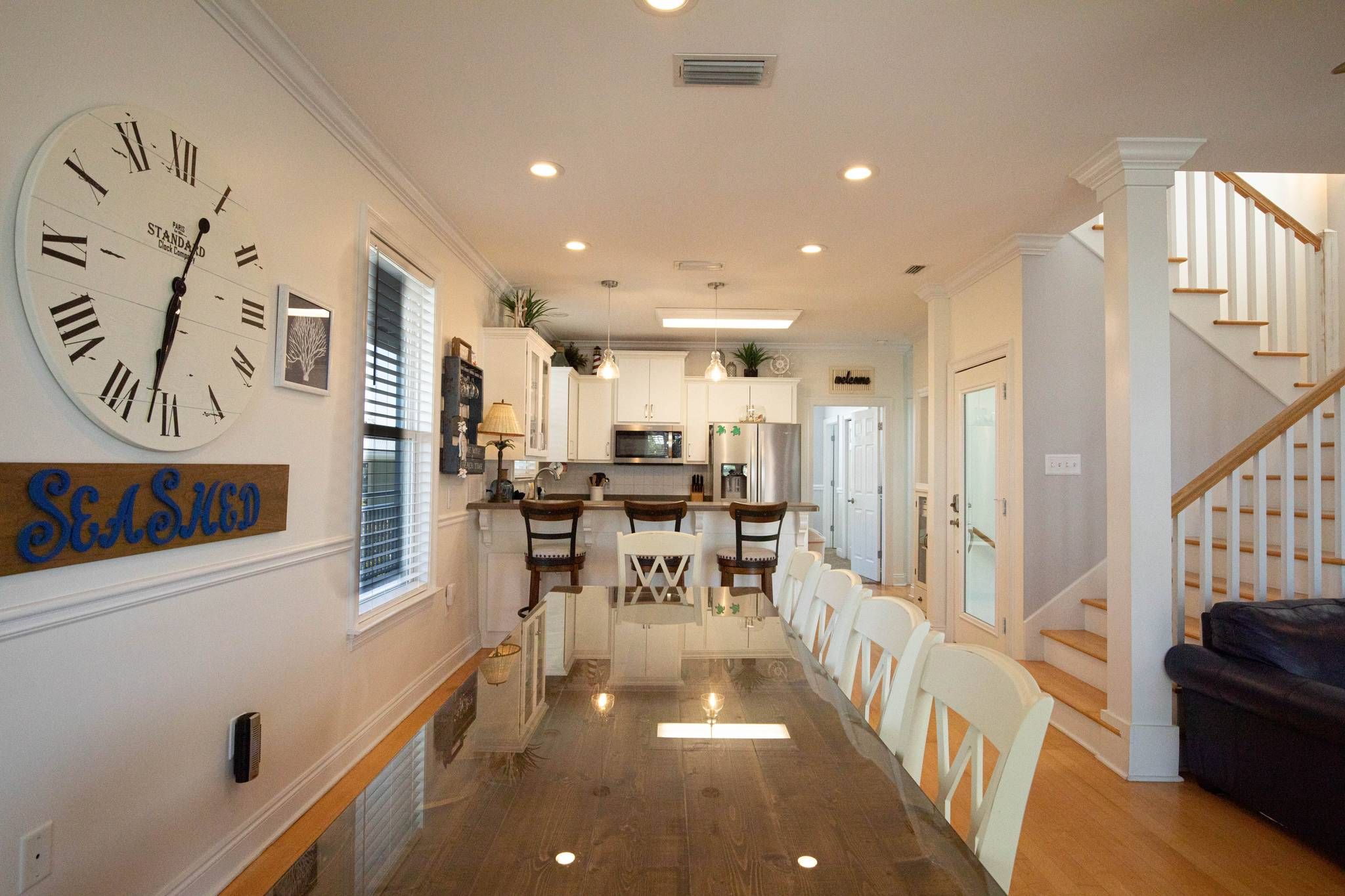 A spacious kitchen with a large clock, a dining area with chairs, and a staircase.