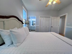 A bedroom with a large bed, a ceiling fan, and a bathroom visible through an open door. - Welcome to Sea Shed – Private Pool, Fire Pit, Pet Friendly (Cape San Blas)