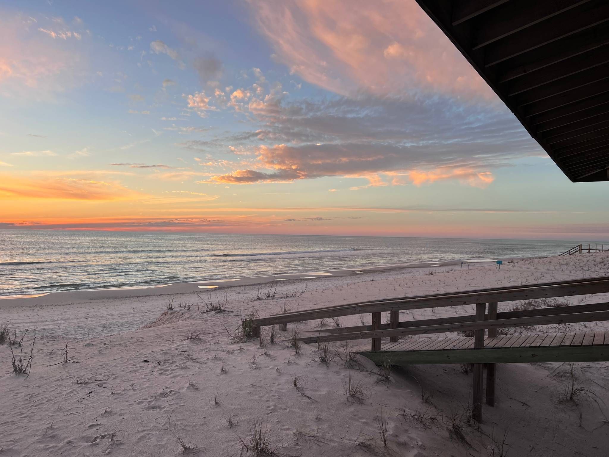 Une plage avec une promenade en bois menant au rivage, d’où l’on peut admirer l’océan au coucher du soleil.