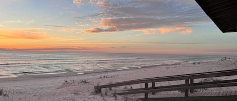 A beach with a wooden walkway leading to the shore, overlooking the ocean during sunset.