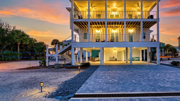 A two-story building with a covered outdoor area, multiple balconies, and a driveway leading to a parked car. - Lulu's Beach House- Volleyball Court, North Cape (Port St Joe)