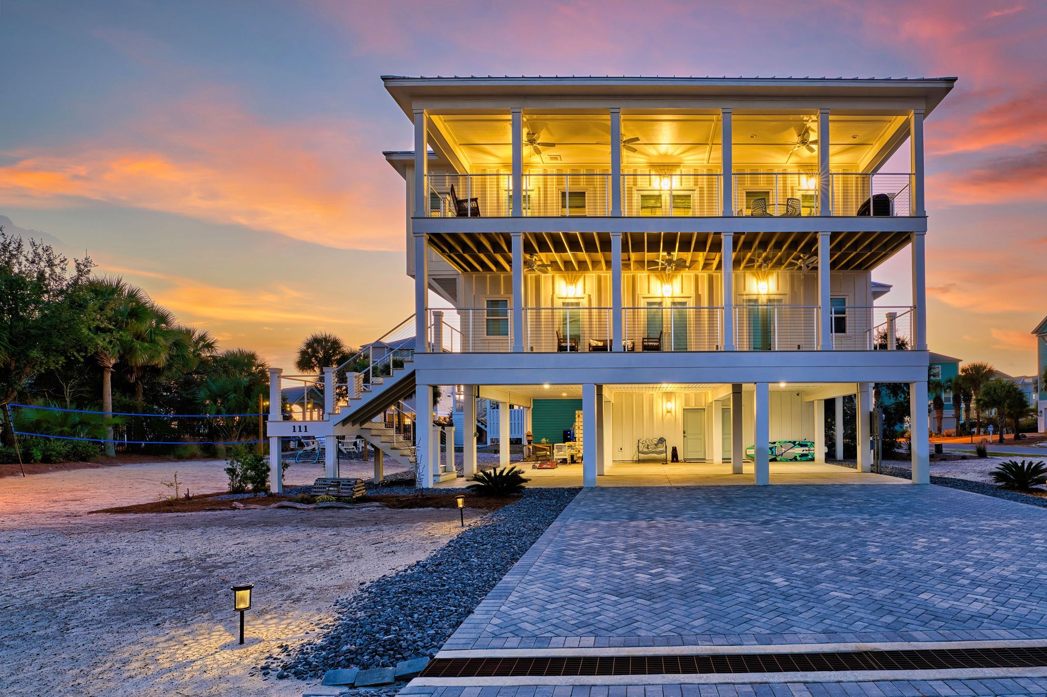 A two-story building with a covered outdoor area, multiple balconies, and a driveway leading to a parked car.