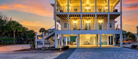 A two-story building with a covered outdoor area, multiple balconies, and a driveway leading to a parked car.