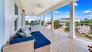 A covered outdoor area with a wicker sofa and blue cushions, a dining table with chairs, and a view of surrounding buildings. - Lulu's Beach House- Volleyball Court, North Cape (Port St Joe)