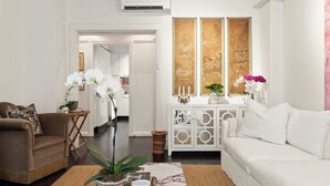 A living room with a brown sofa, white sofa, and a coffee table with decorative items. There is a white cabinet with glass doors and a painting on the wall.