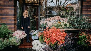 A person standing at the entrance of a building with a variety of flowers displayed outside.