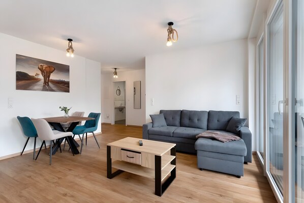 A modern living room with a sofa, a dining table with chairs, a coffee table, and a painting on the wall.