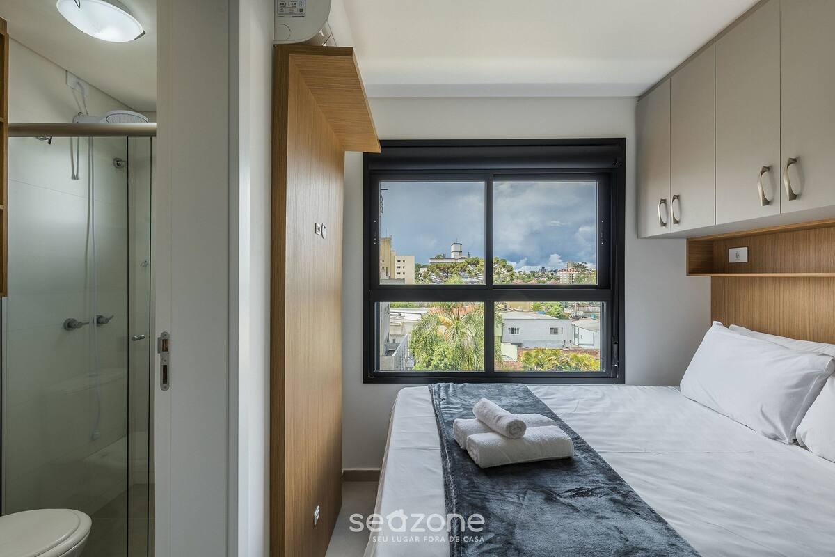 Ein modernes Hotelzimmer mit einem großen Fenster, einer Dusche und einem Bett mit weißer Bettwäsche.
