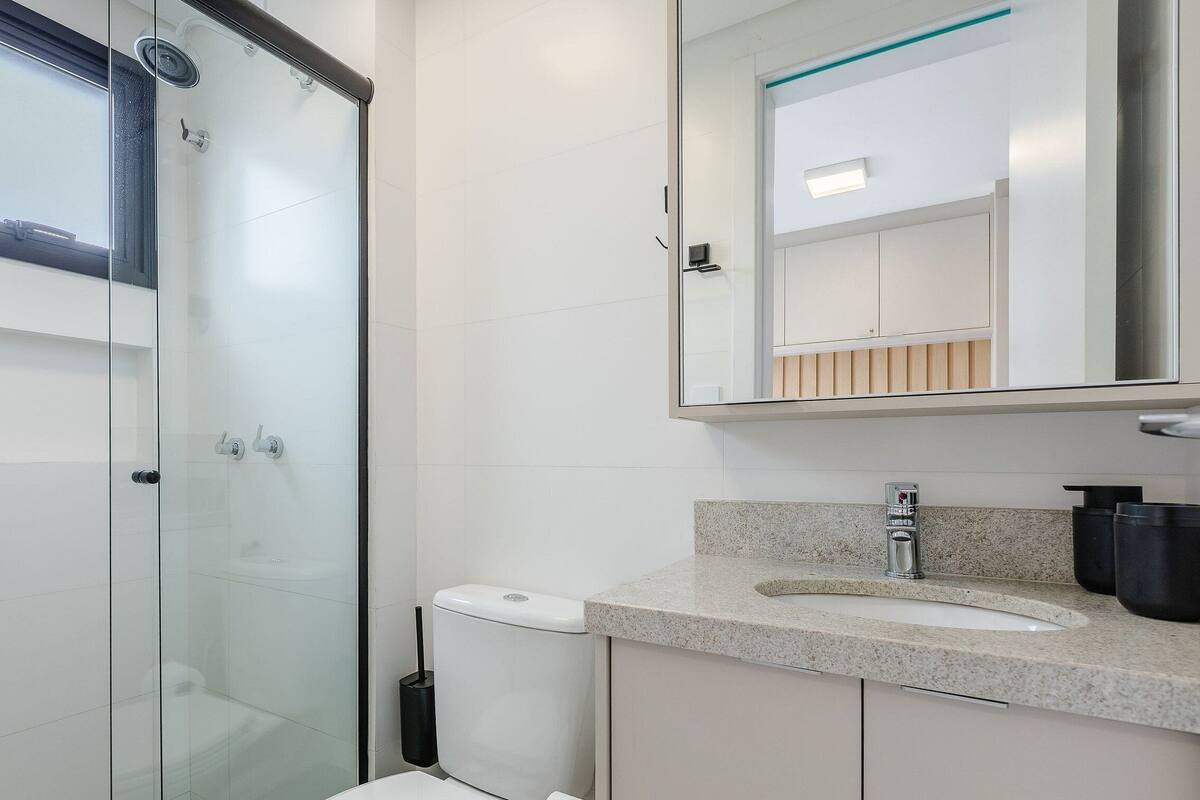 Ein modernes Badezimmer mit Duschkabine aus Glas, einer weißen Toilette und einer Waschtischplatte aus Granit mit Waschbecken und Spiegel.