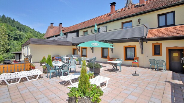 A courtyard with outdoor seating, a green umbrella, and a mountain backdrop. - Hotel Restaurant Freihof (Oberharmersbach)