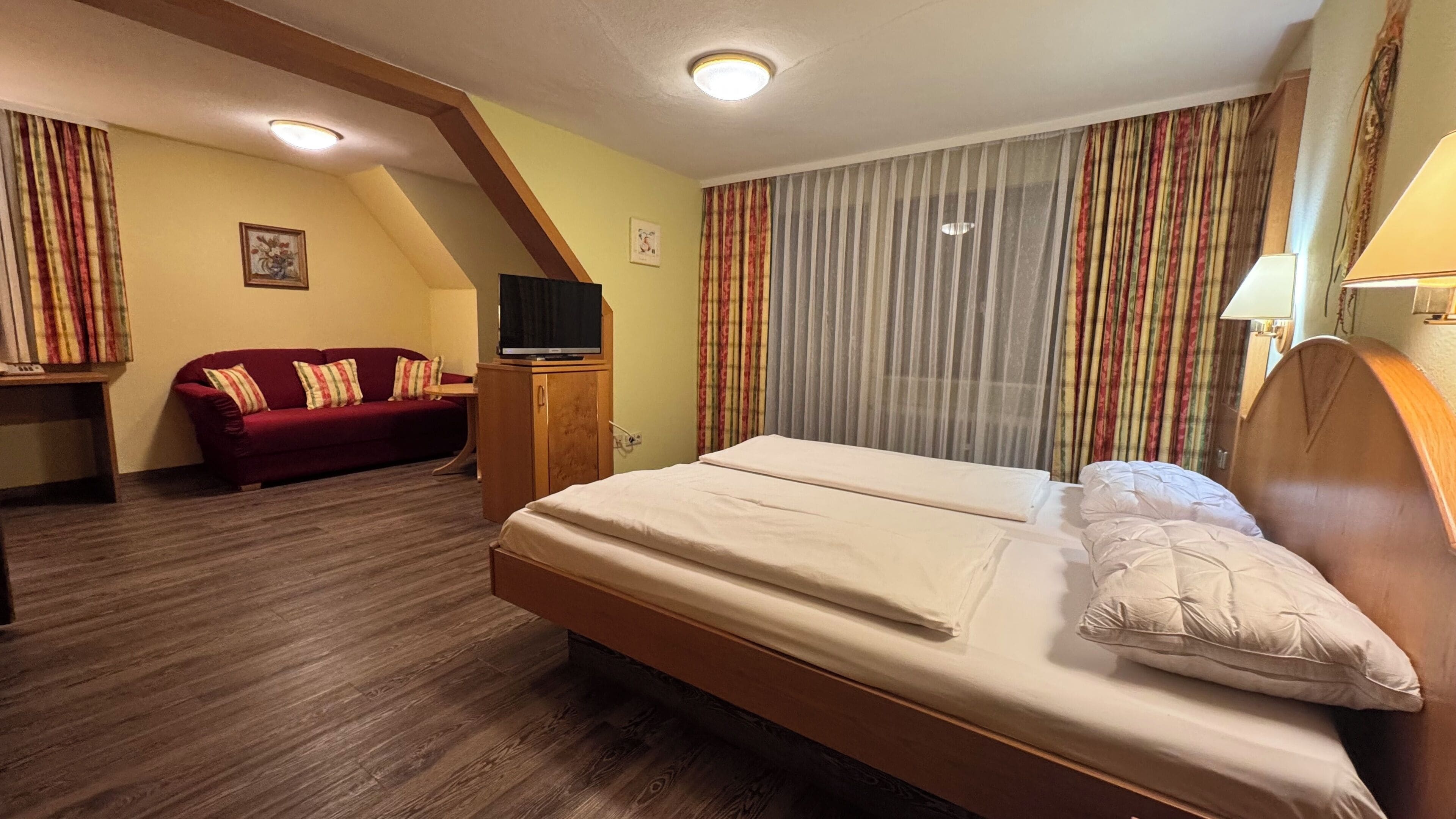 A hotel room with a bed, a red sofa, a wooden cabinet, and a television.