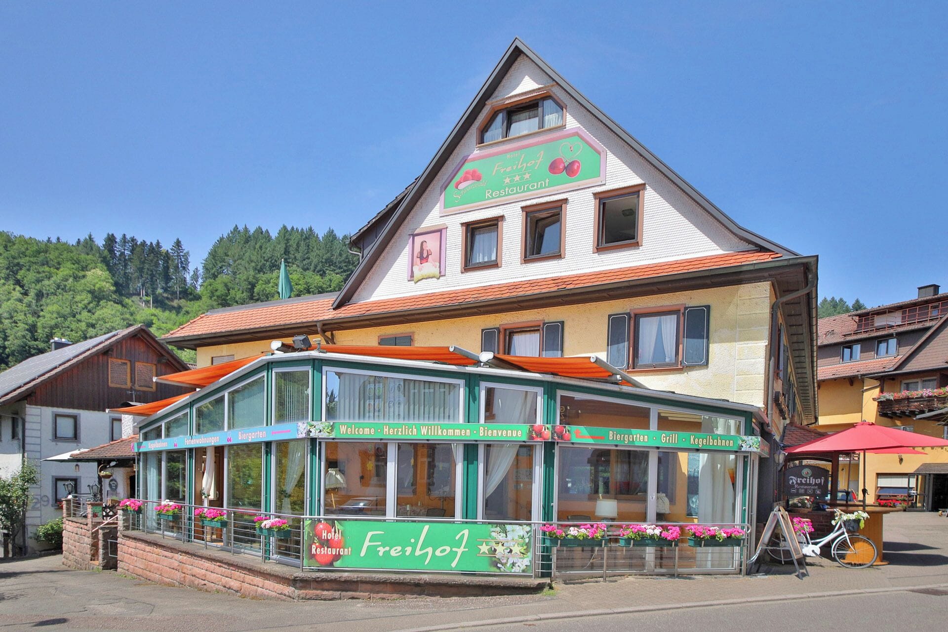 Un edificio tradicional con toldo verde, un letrero que indica que es un hotel y restaurante, y un cielo despejado.