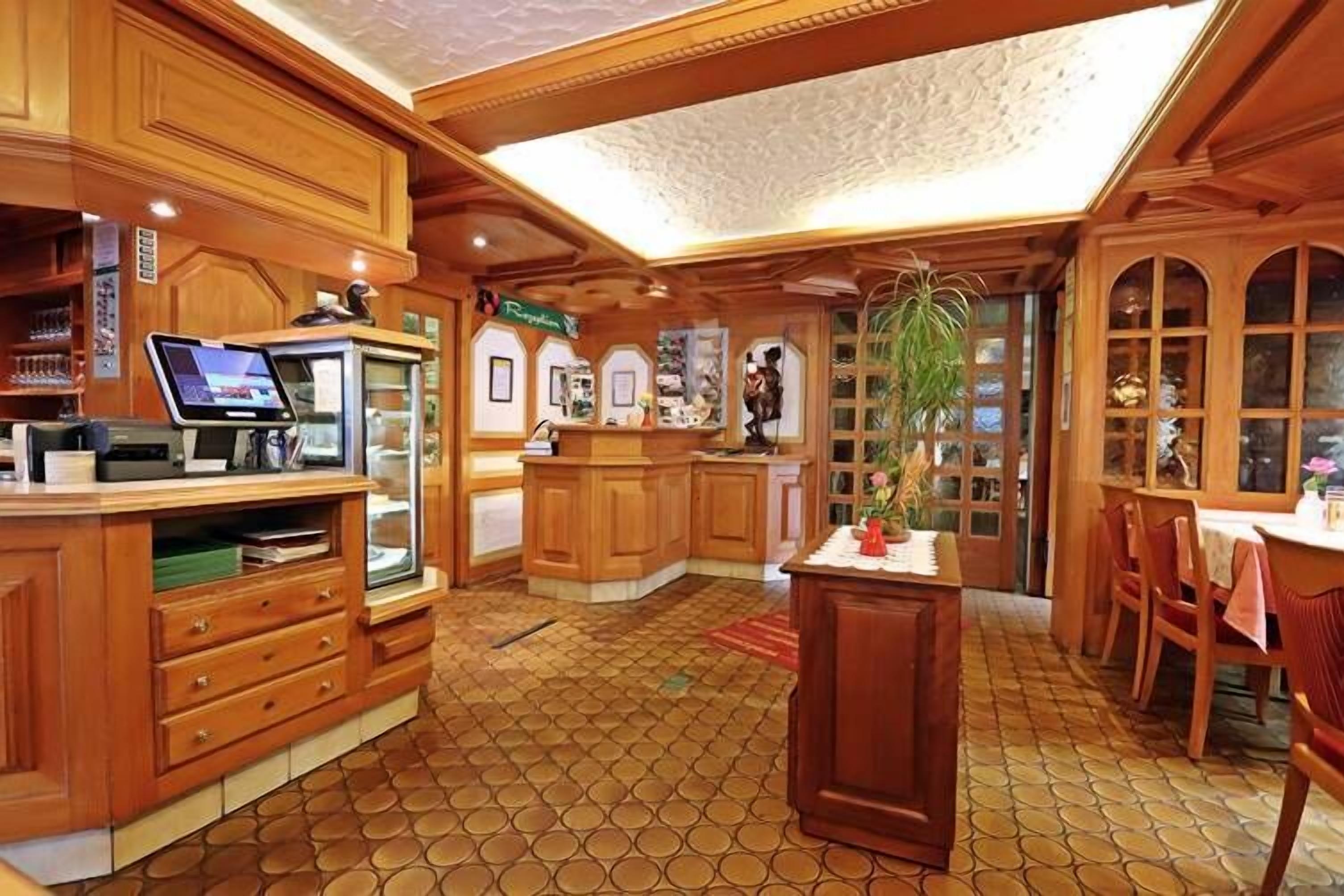 A wooden interior with a reception desk, a digital screen, and a tiled floor.