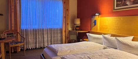 A hotel room with a bed, a desk with a chair, a lamp, and a painting on the wall.