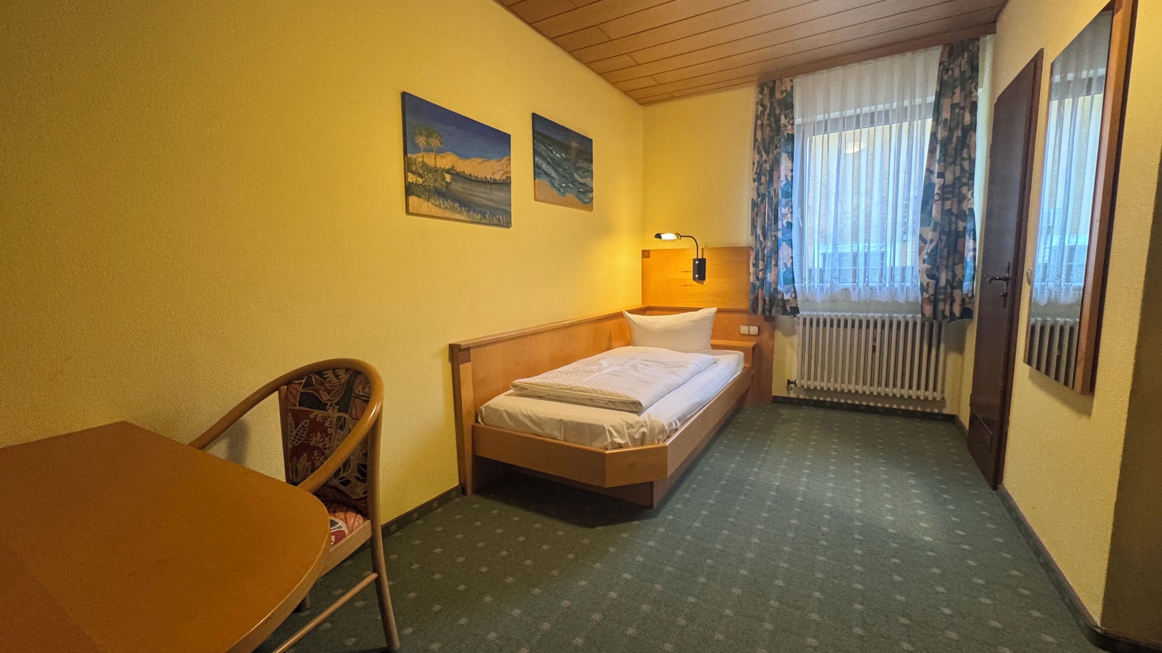 Habitación de hotel con una cama, una silla, una mesa y dos cuadros en la pared.