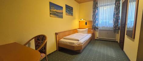 Habitación de hotel con una cama, una silla, una mesa y dos cuadros en la pared.