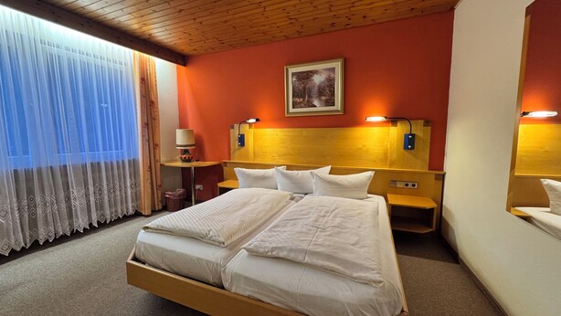 A hotel room with a large bed, two bedside tables, a nightstand, a lamp, and a painting on the wall. - Hotel Restaurant Freihof (Oberharmersbach)