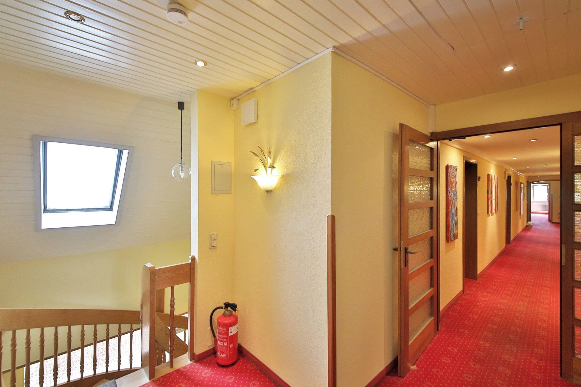 A hotel corridor with a red carpet, wooden doors, and a fire extinguisher.