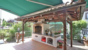 An outdoor patio with a stone-built barbecue area, a green awning, and potted plants. - Hotel Restaurant Freihof (Oberharmersbach)