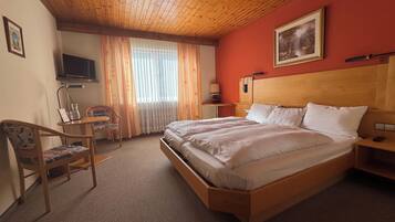 Een hotelkamer met een houten bed, een bureau met stoel, een televisie en een schilderij aan de muur.