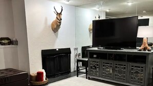 Una sala de estar con un trofeo de caza en la pared, una chimenea, un televisor sobre un mueble y una lámpara.