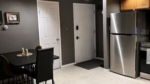 Una cocina compacta con un refrigerador de acero inoxidable, una mesa de comedor con sillas y dos puertas blancas.