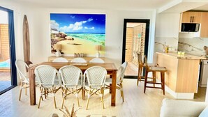 Una sala moderna con comedor, cocina y un amplio mural con temática playera.