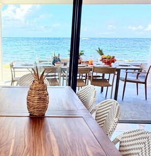 An outdoor dining area with a view of the ocean, wooden tables, wicker chairs, and a woven centerpiece.