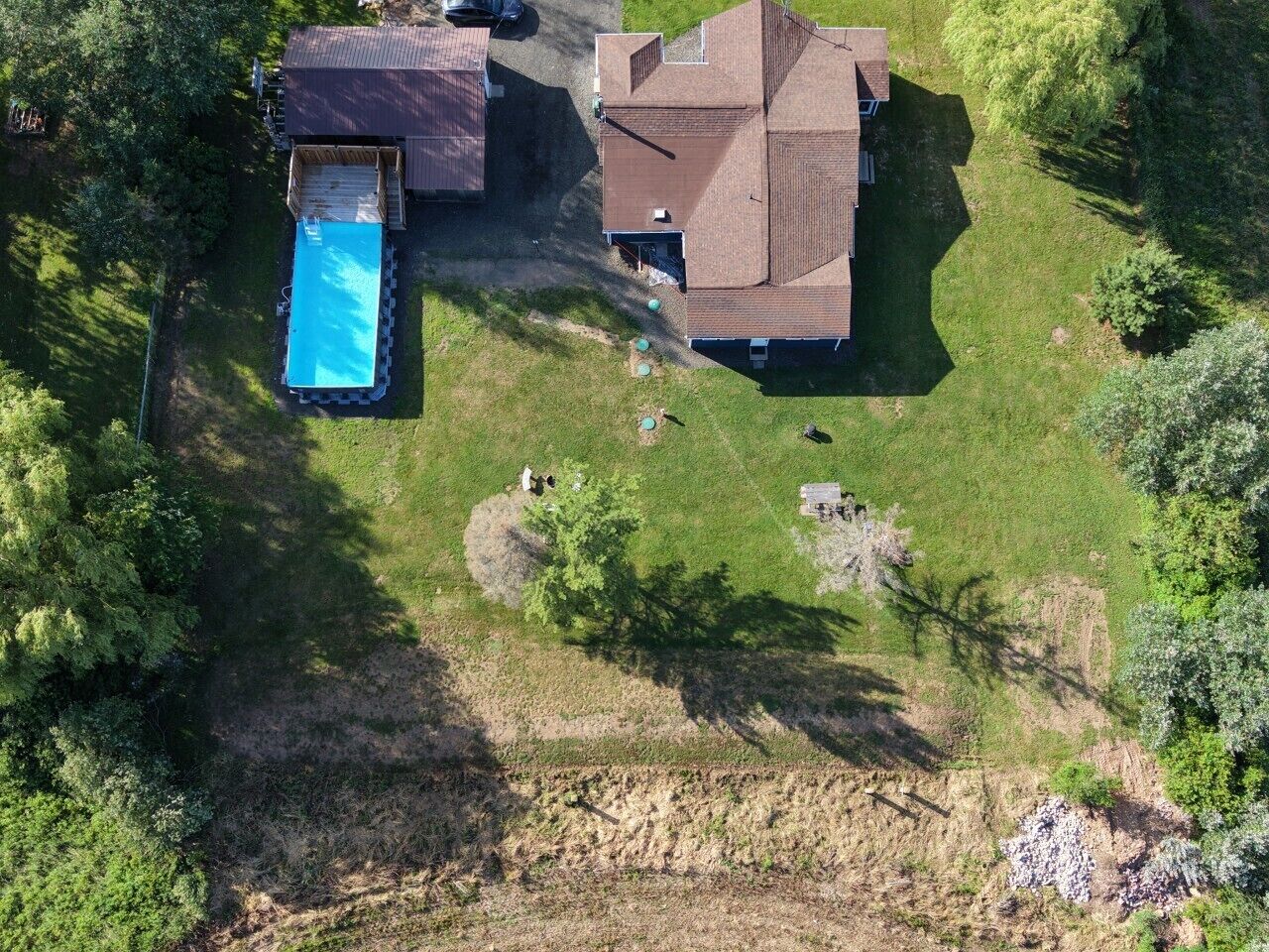 An aerial view of a house with a swimming pool, surrounded by a grassy yard and trees.