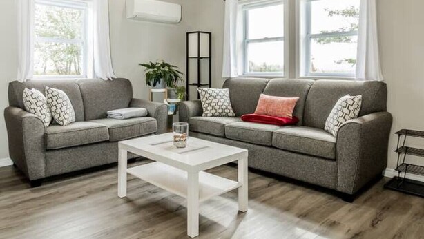 A living room with two grey sofas, a white coffee table, wooden beams on the ceiling, and large windows with white curtains. - Elegant home away from home - Valley View (Brooklyn)