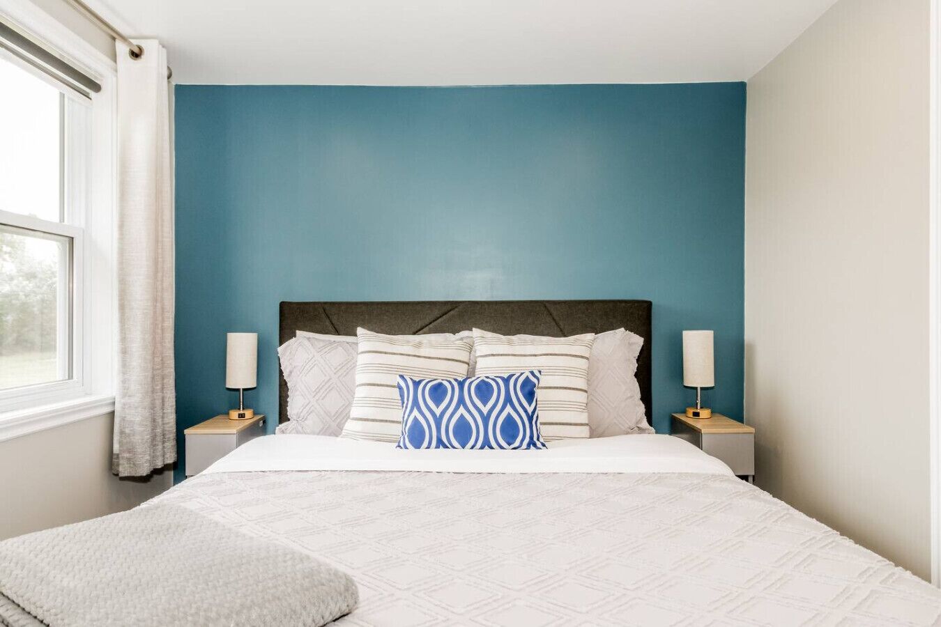 Een slaapkamer met een bed, twee nachtkastjes, een raam met gordijnen en een blauwe muur.