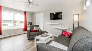A modern living room with a grey sofa, a white coffee table, a grey armchair, and a red curtain.