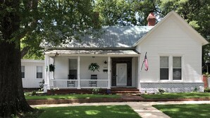 A single-story white house with a front porch, a brick foundation, and a small front yard. - Jacklin Cottage at Generals' Quarters (Corinth)