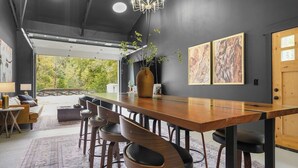 A modern dining area with a long wooden table, six bar stools, and a vase with greenery.