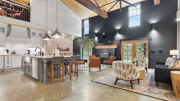 A spacious kitchen with a central island, a dining area with chairs, a fireplace, and a living room with sofas and a coffee table.