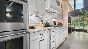 A modern kitchen with white cabinetry, a stainless steel oven, and a large window overlooking a garden.
